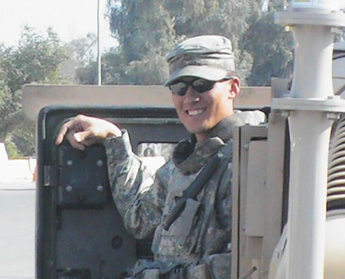 Steve stands in his army fatigues next to a Humvee