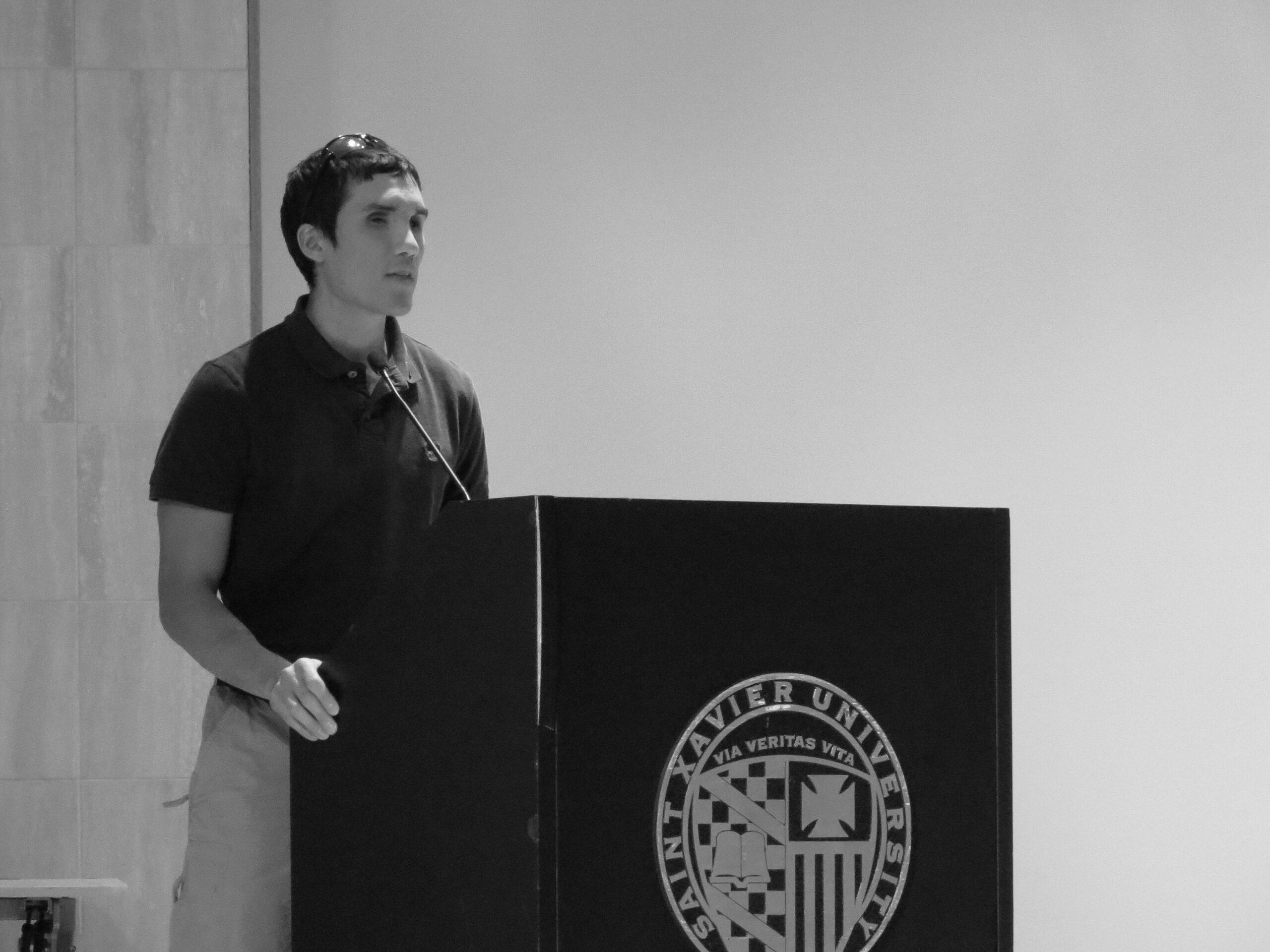 Steve Baskis stands behind a podium while speaking to St Xavier University