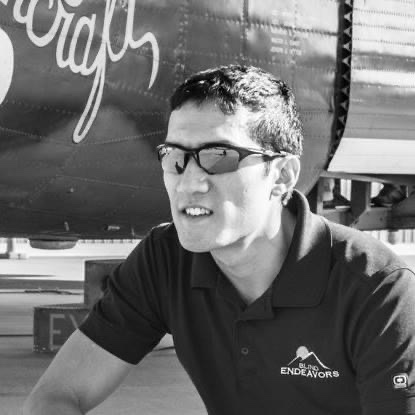 A black and white photo of Steve Baskis kneeling in front of a B-24 Liberator, the same type of plane that his grandfather flew in during WWII.